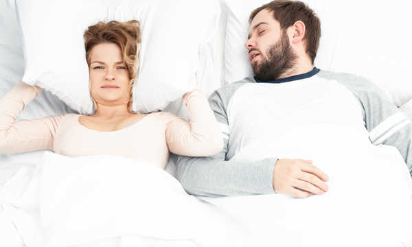 Kobieta zakrywa uszy poduszką z powodu chrapania partnera Kobieta zakrywa uszy poduszką z powodu chrapania partnera