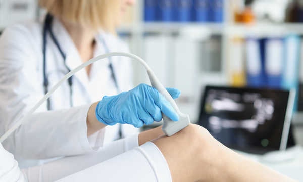 Lekarz ortopeda wykonuje badanie ultrasonograficzne kolana pacjenta w gabinecie Lekarz ortopeda wykonuje badanie ultrasonograficzne kolana pacjenta w gabinecie